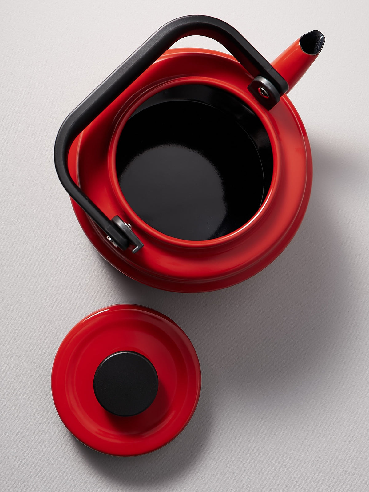 An Amu Stove-top Kettle - Red with a black lid on a white surface.