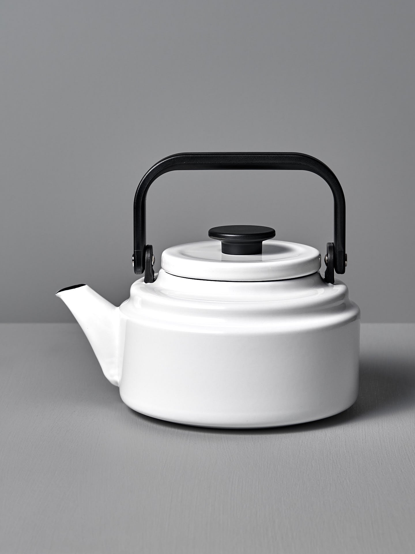 A white Amu Stove-top Kettle with a black handle on a grey background. (Brand: Noda Horo)
