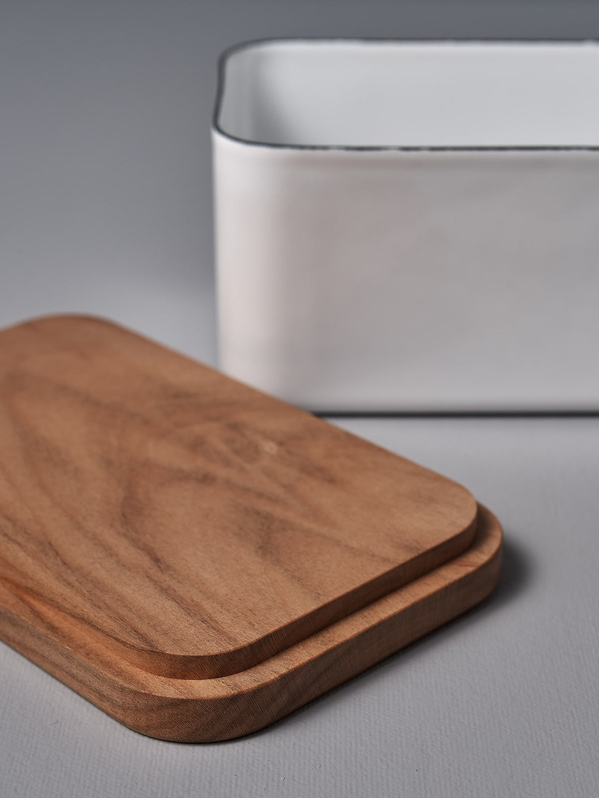 A Noda Horo Enamel Butter Case – 450g and a white bowl on a grey surface.