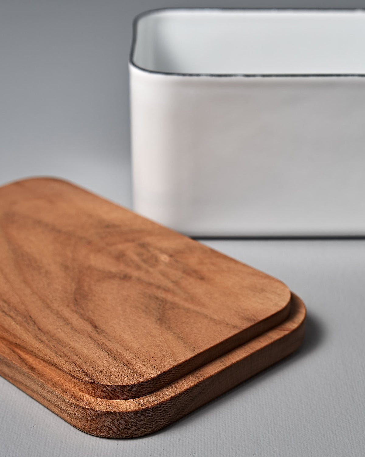 A Noda Horo Enamel Butter Case – 450g and a white bowl on a grey surface.