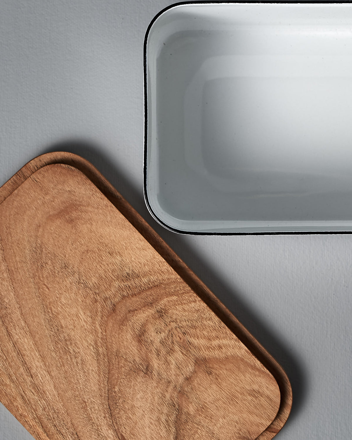 An Enamel Butter Case - 450𝚐 from Noda Horo and a wooden tray on a grey surface.