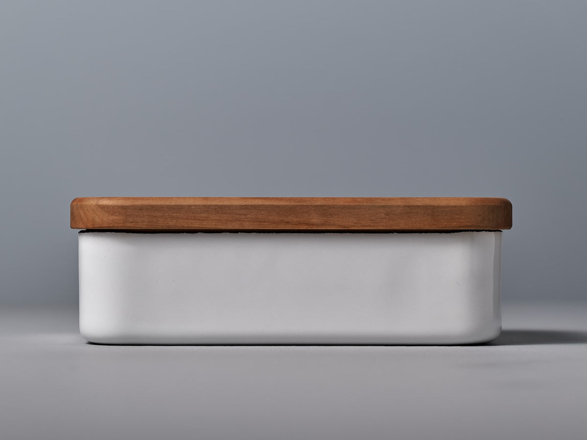 A white Enamel Butter Case - 200𝚐 with a wooden lid on a grey background by Noda Horo.