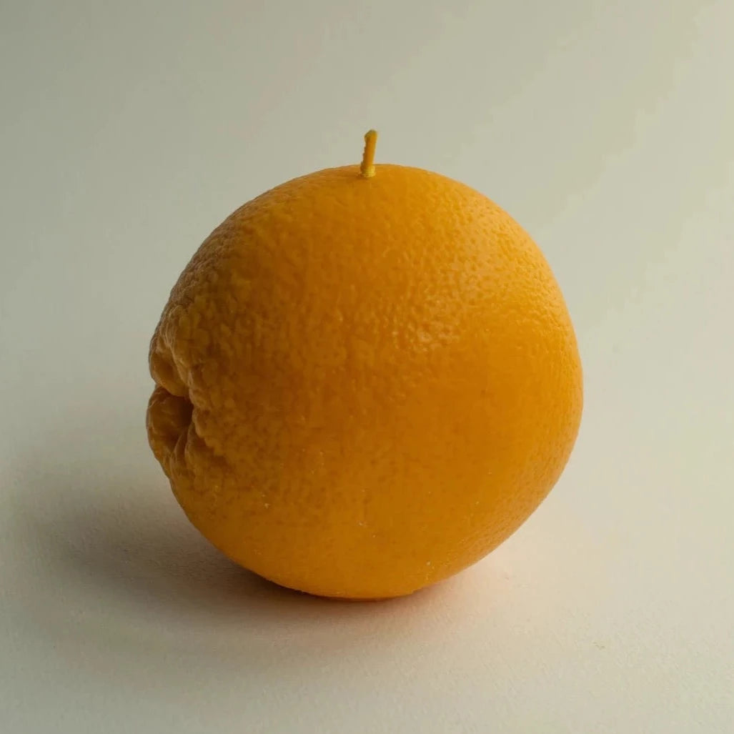 An Orange Candle from Nonna&#39;s Grocer on a white surface.