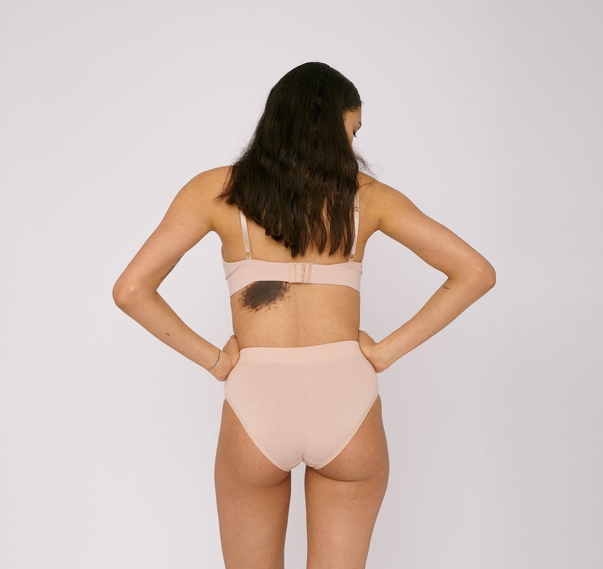 The back view of a woman wearing Organic Basics Bikini Briefs ⋅ organic cotton (2-pack) – Rose Nude.