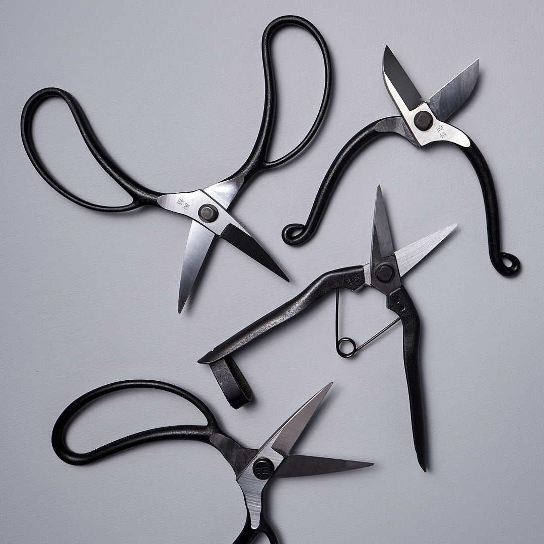 Four pairs of Okatsune Ikebana Scissors №213 on a gray surface.