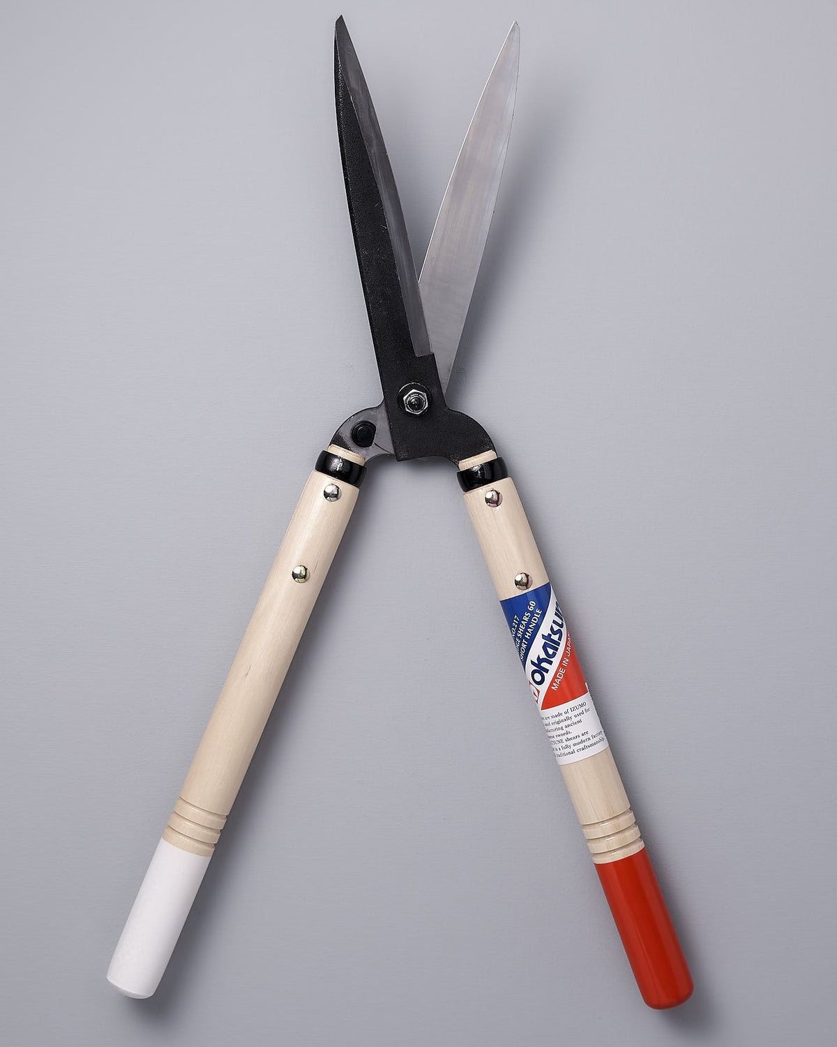 A pair of Okatsune Japanese Hedge Shears №217 – Short Handled with a red, white and blue handle.