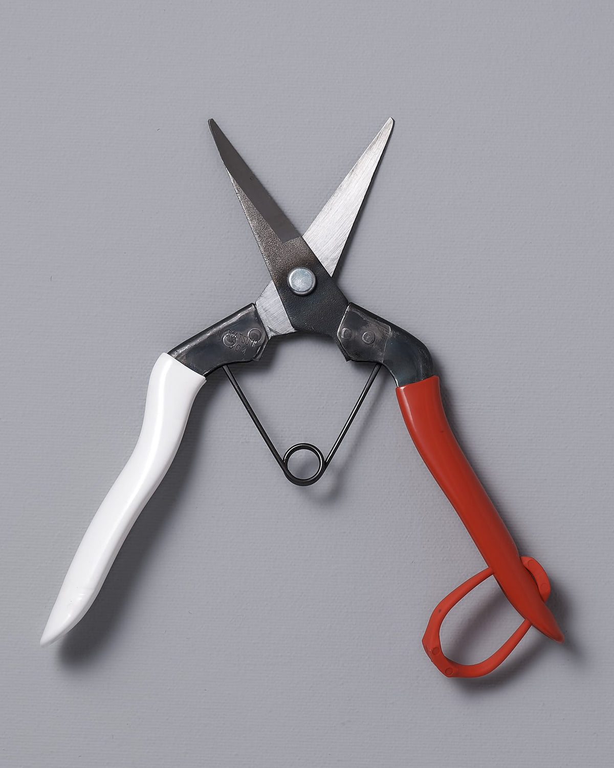 A pair of Okatsune Japanese Snips №304 with a red handle on a gray surface.