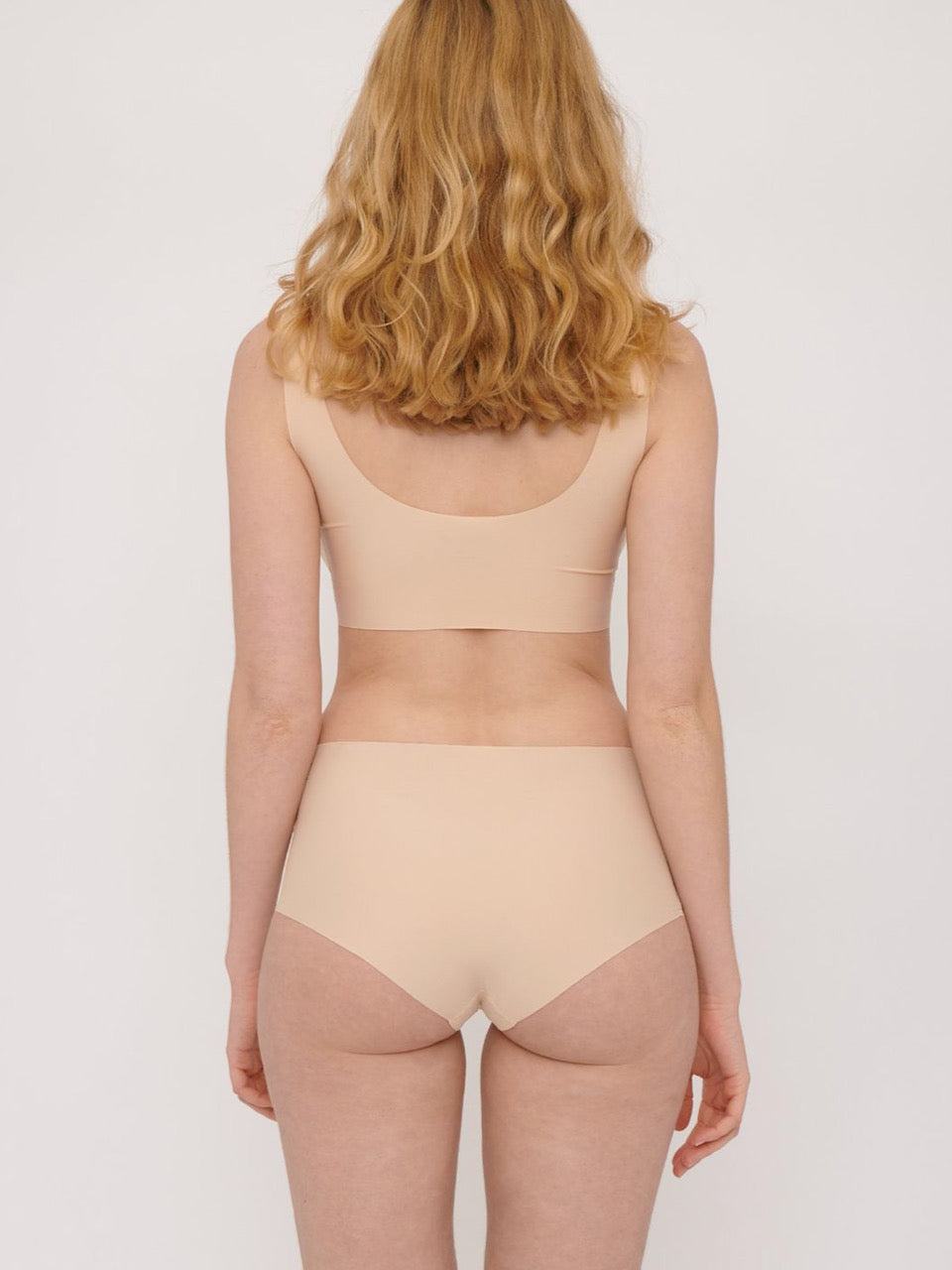 The back view of a woman in Organic Basics&#39; Invisible Cheeky High-Rise Briefs (2-pack) – Oak bikini.