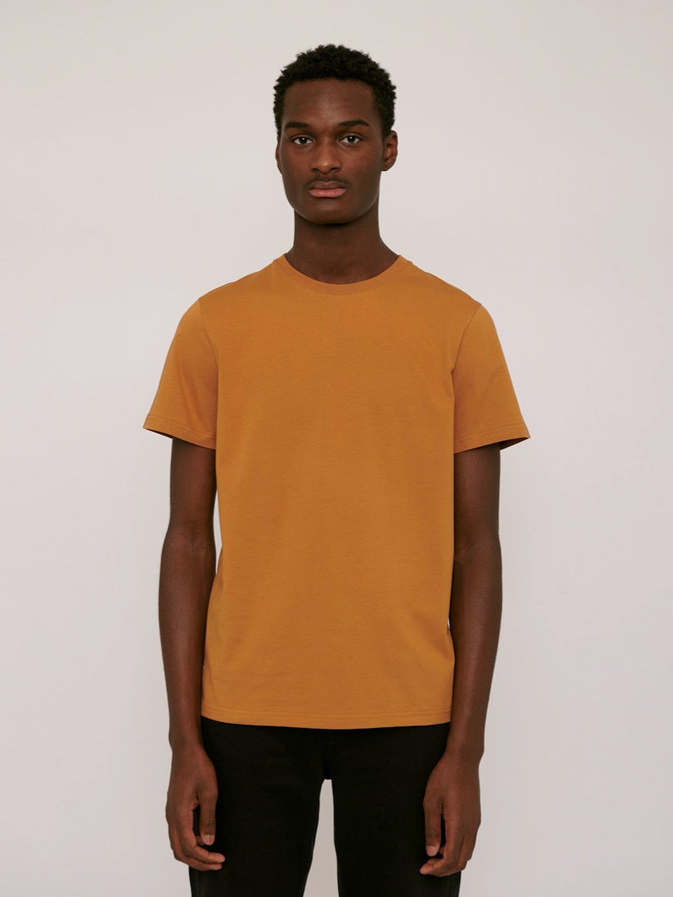 The model is wearing an Organic Basics Tee ⋅ organic cotton – Ocher.