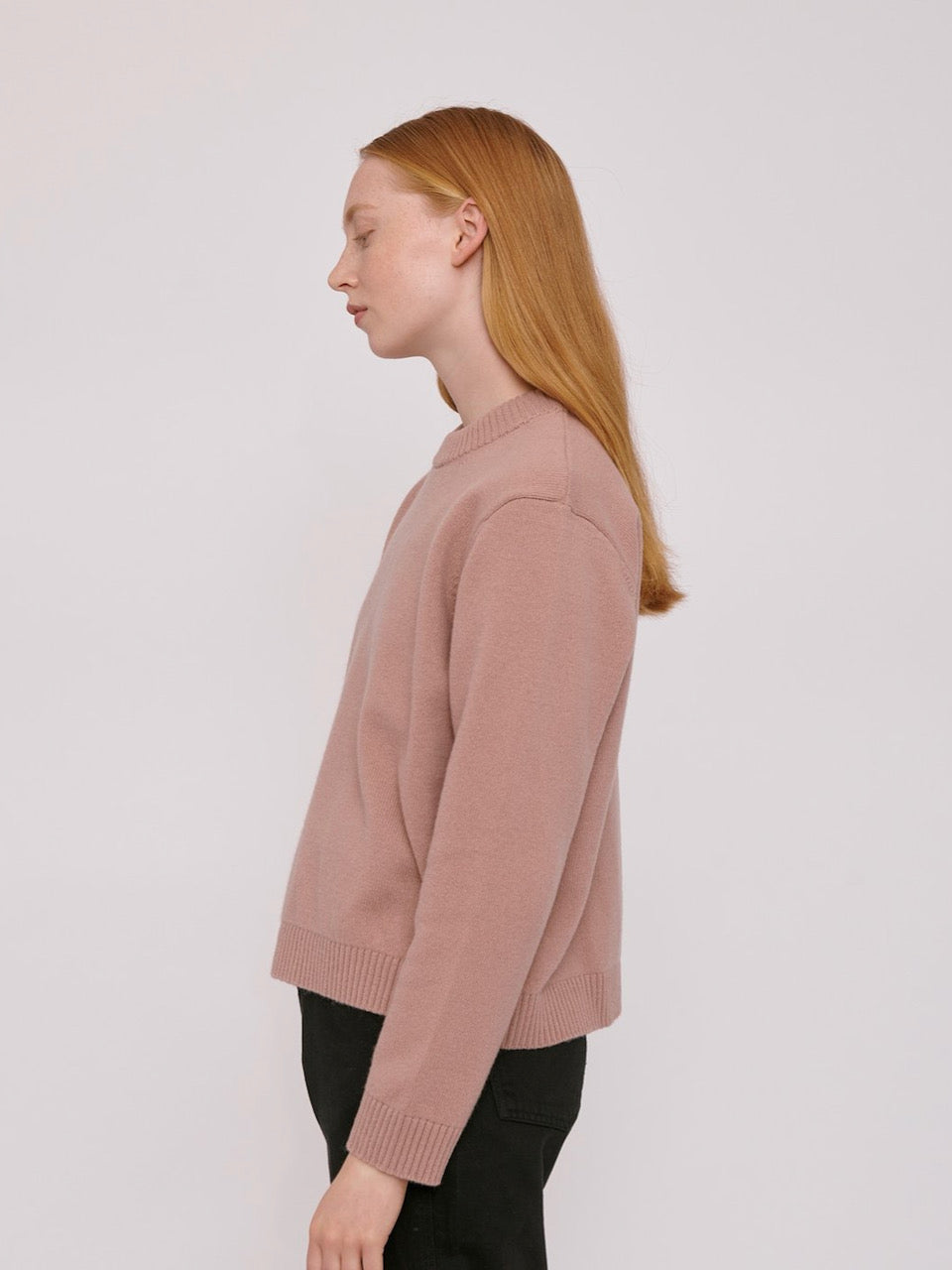 The model is wearing a Recycled Wool Boxy Knit Jumper - Dusty Rose by Organic Basics and black pants.