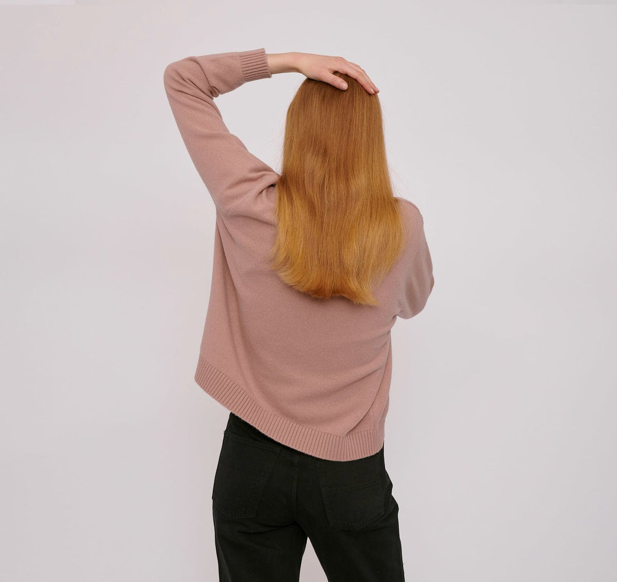 A woman wearing an Organic Basics Recycled Wool Boxy Knit Jumper - Dusty Rose and black pants.