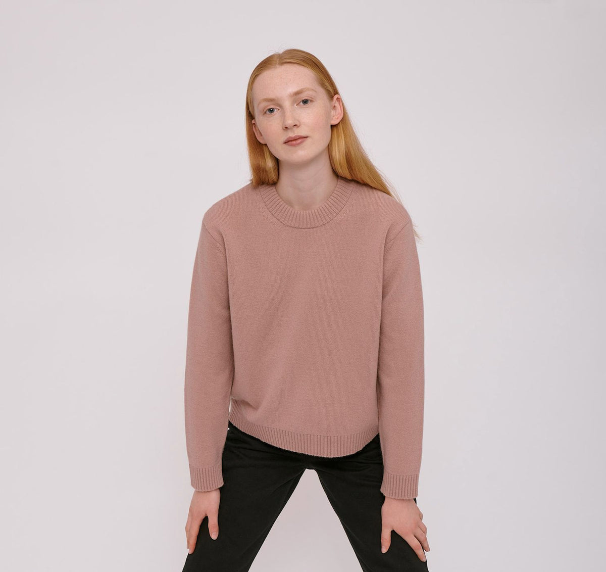 The model is wearing an Organic Basics Recycled Wool Boxy Knit Jumper in Dusty Rose and black pants.