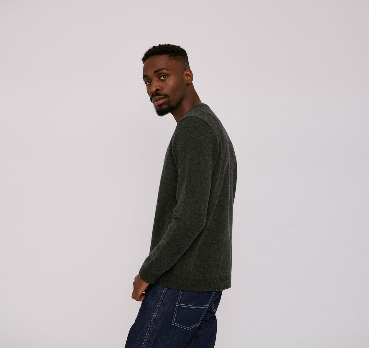 A man wearing an Organic Basics Recycled Wool Knit Jumper - Charcoal Melange sweater and jeans.