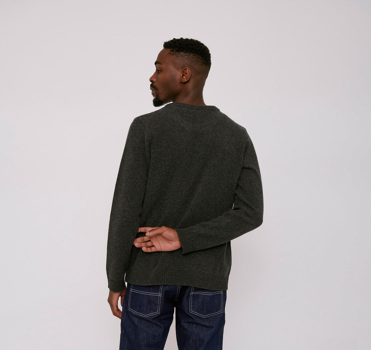 The back of a man wearing an Organic Basics Recycled Wool Knit Jumper – Charcoal Melange sweater and jeans.