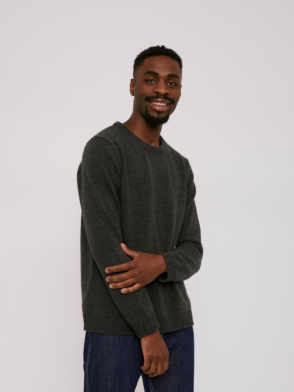 A man in a grey Recycled Wool Knit Jumper – Charcoal Melange from Organic Basics is posing for a photo.