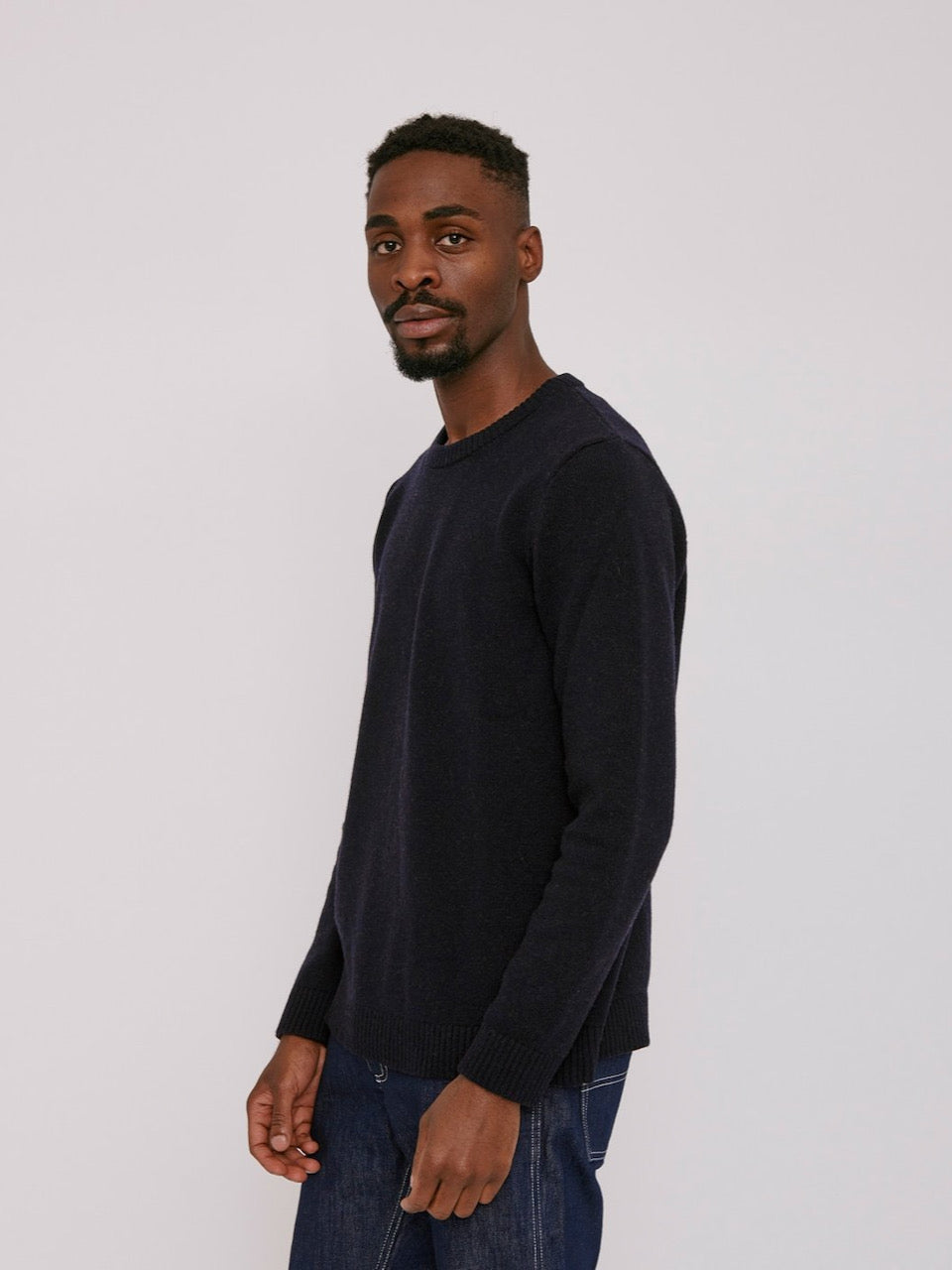 The model is wearing an Organic Basics Recycled Wool Knit Jumper – Navy and jeans.