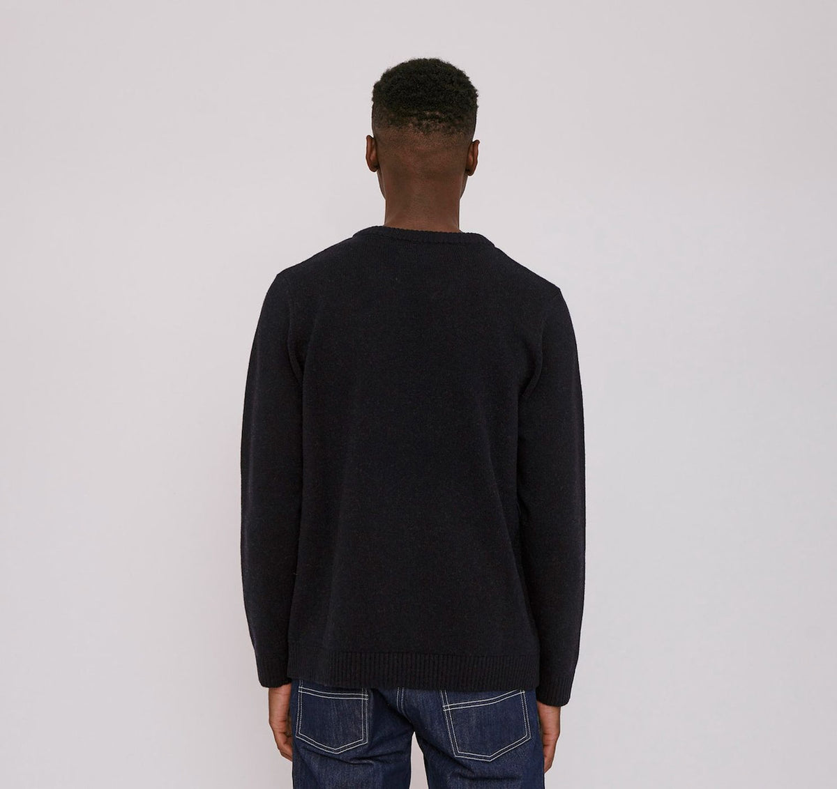 The back view of a man wearing an Organic Basics Recycled Wool Knit Jumper - Navy and jeans.