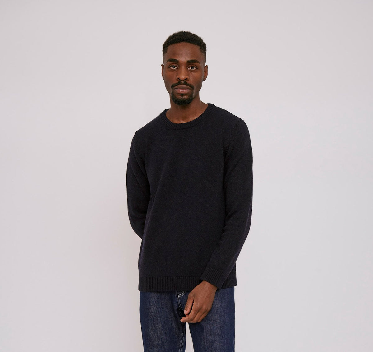The model is wearing an Organic Basics Recycled Wool Knit Jumper – Navy and jeans.