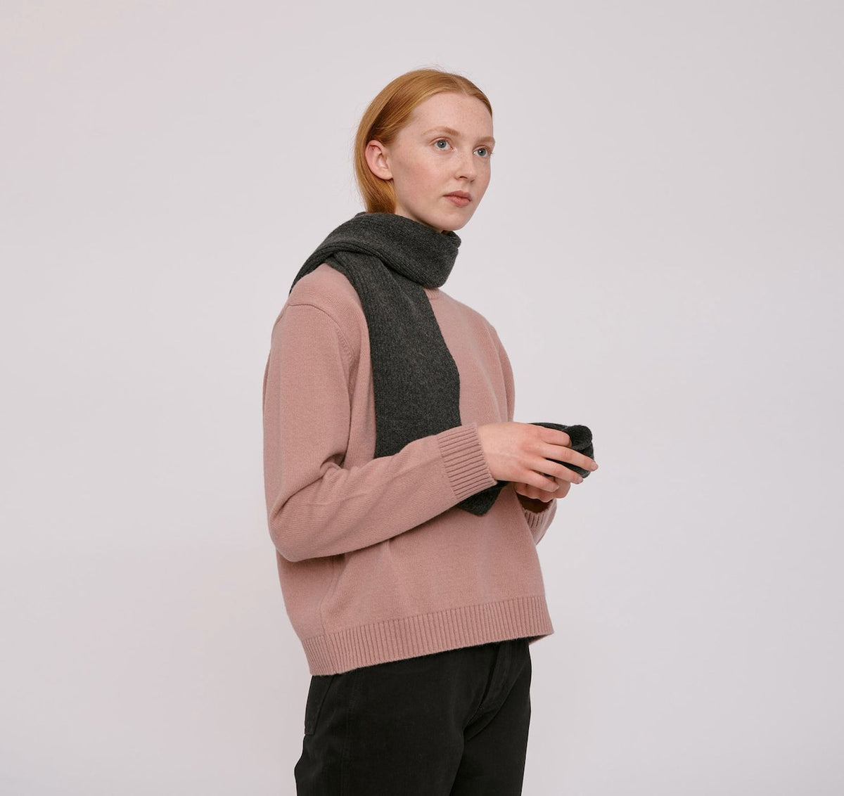 The model is wearing a Recycled Wool Scarf – Charcoal Melange by Organic Basics and black pants.