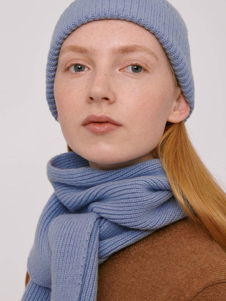 A woman wearing an Organic Basics Recycled Wool Scarf - Light Blue and a blue knitted hat.