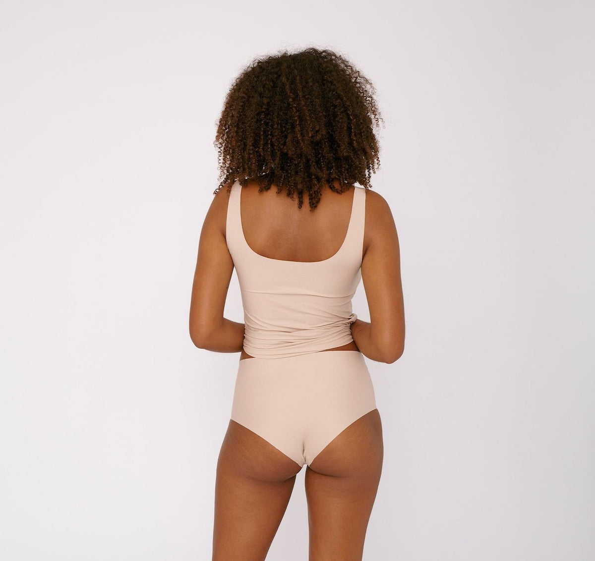 The back view of a woman wearing Organic Basics&#39; Invisible Cheeky High-Rise Briefs (2-pack) – Rose Nude bikini.