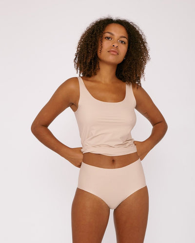 A woman in Organic Basics' Invisible Cheeky High-Rise Briefs (2-pack) - Rose Nude tank top and panties.