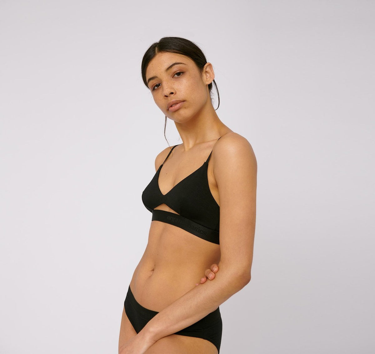 The model is wearing an Organic Basics TENCEL™ Lite Bralette – Black bikini top.