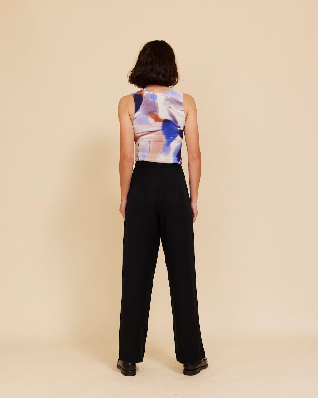 The back view of a woman wearing an OVNA OVICH black top and Me Time Trouser – Onyx wide leg pants.