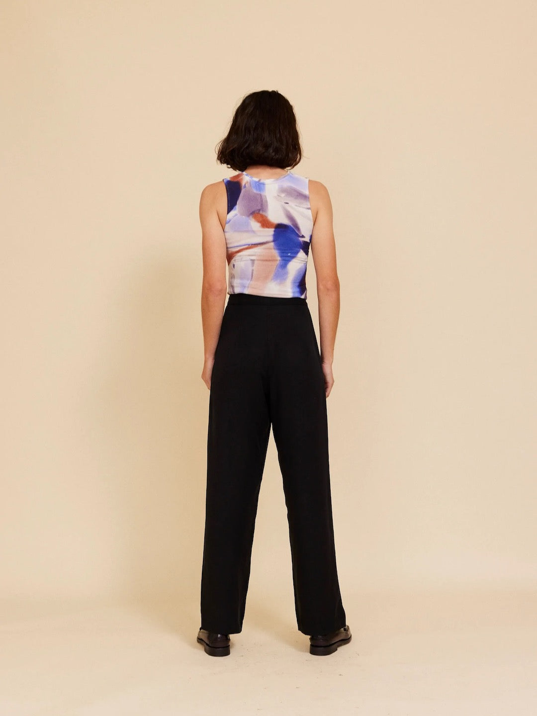 The back view of a woman wearing an OVNA OVICH black top and Me Time Trouser – Onyx wide leg pants.