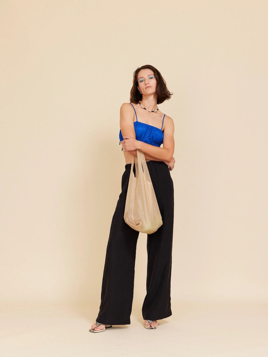 A woman in black pants and a blue top holding a Wander Bag – Champagne by OVNA OVICH.
