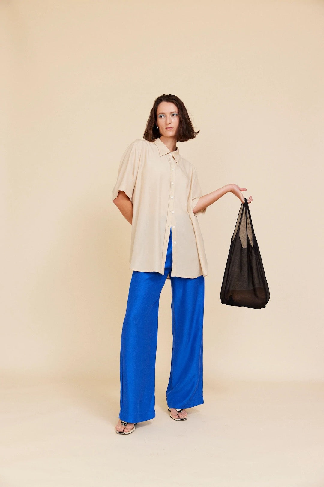 A woman in a tan shirt and blue wide leg pants holding a OVNA OVICH Wander Bag – Onyx.
