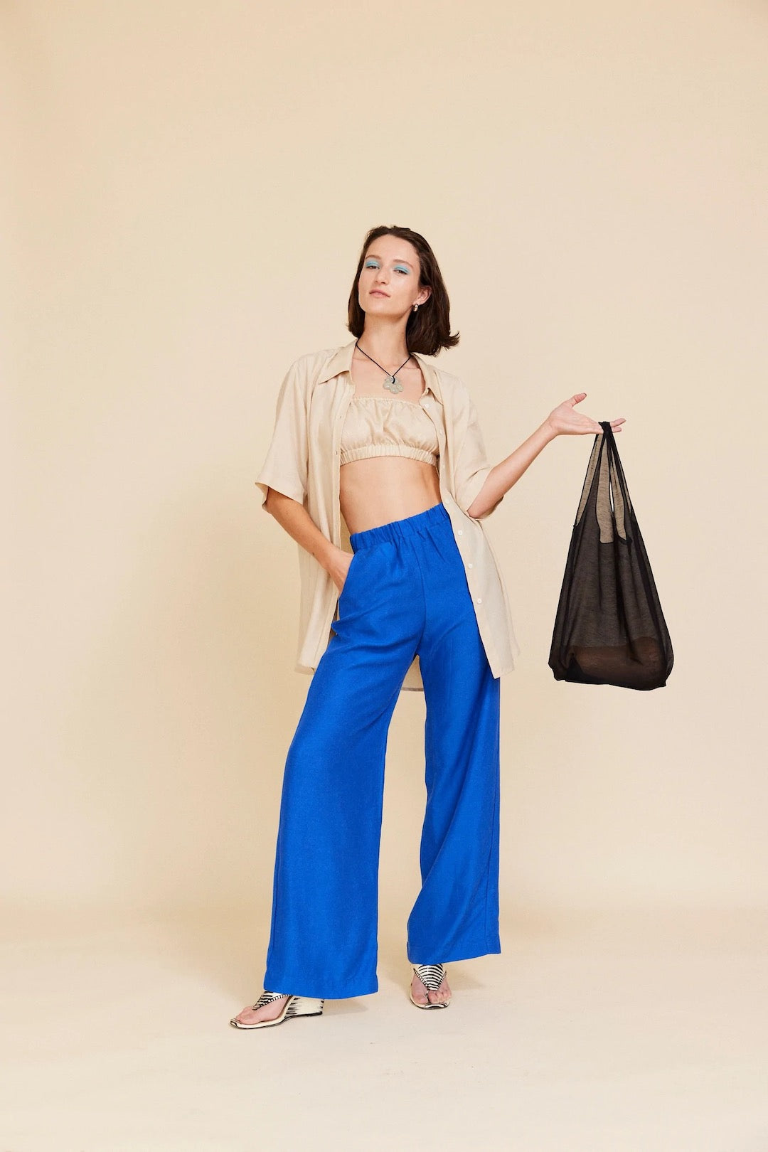 A woman in blue wide leg pants holding a Wander Bag – Onyx shopping bag from OVNA OVICH.
