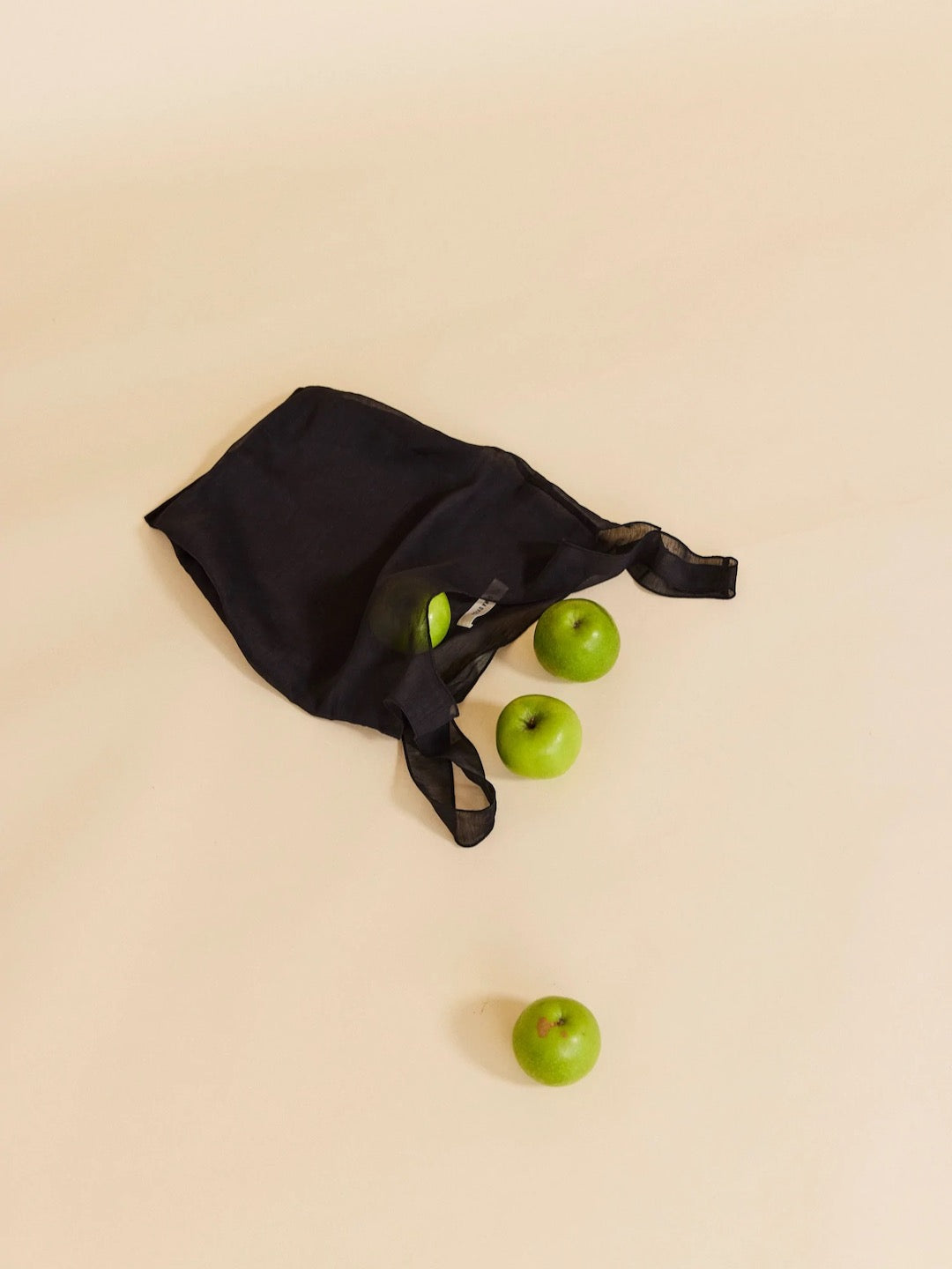 A Wander Bag - Onyx by OVNA OVICH with green apples on it.