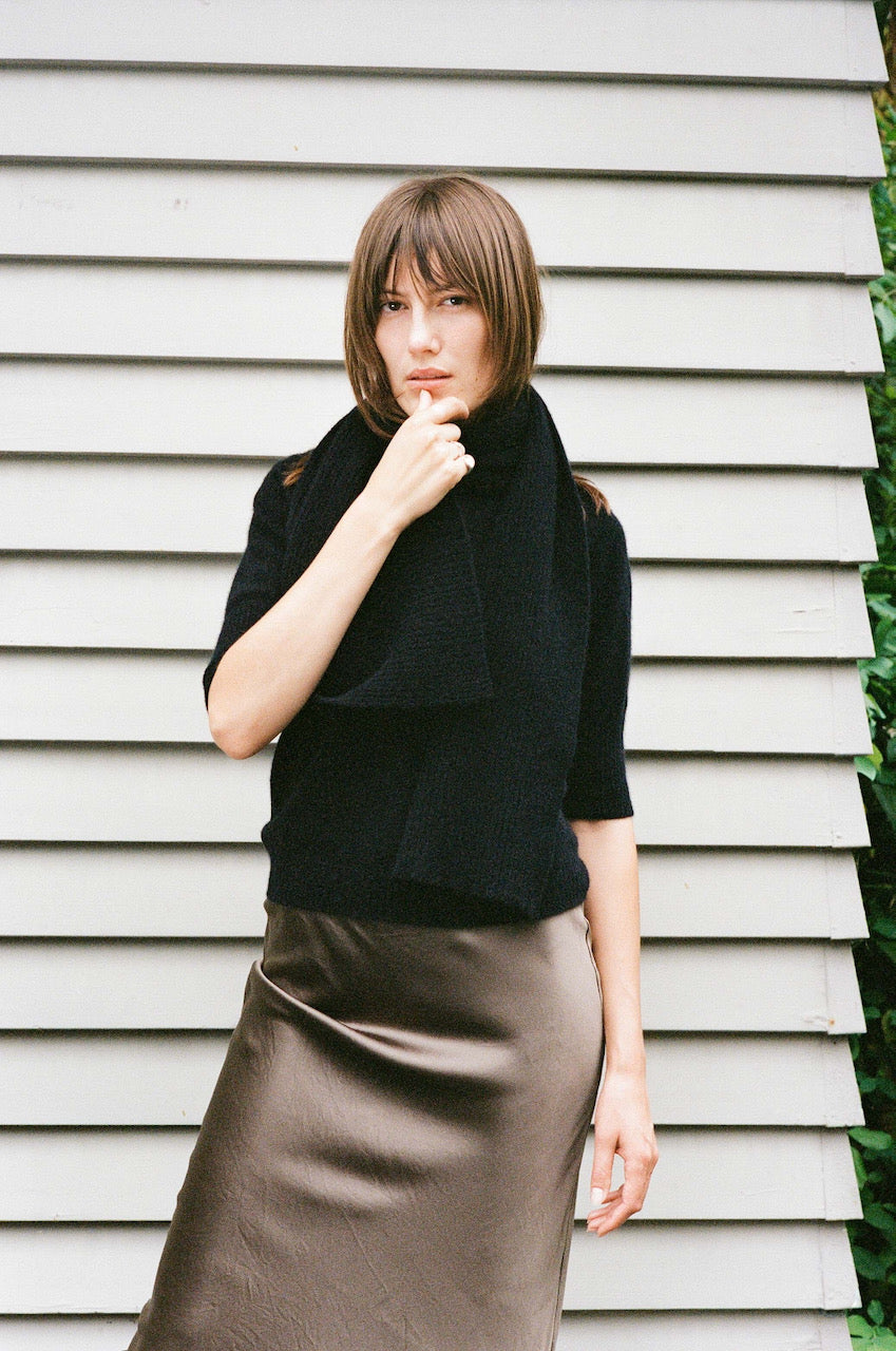 A woman wearing an OVNA OVICH Ra Scarf - Onyx Possum Merino sweater and a brown skirt.