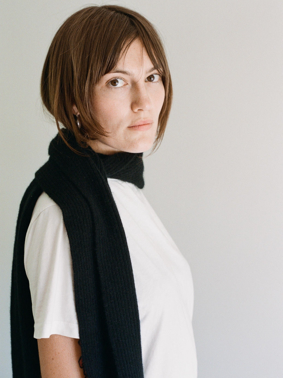 A woman wearing a Ra Scarf - Onyx Possum Merino by OVNA OVICH and a white t - shirt.