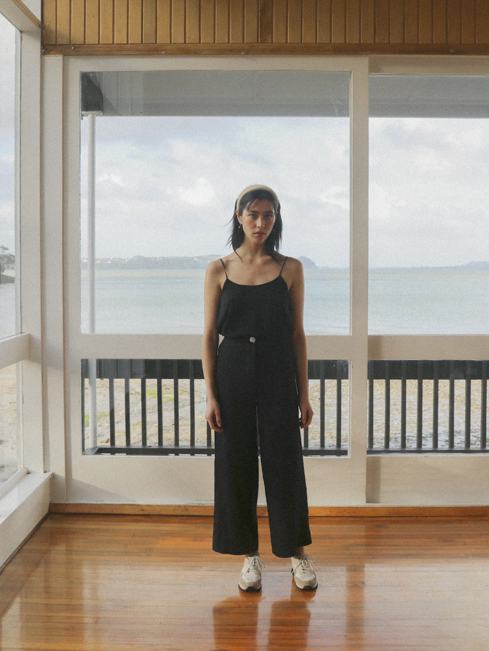 A woman standing in a room with a view of the ocean, wearing OVNA OVICH's Ya Pant - Midnight Black Tencel.