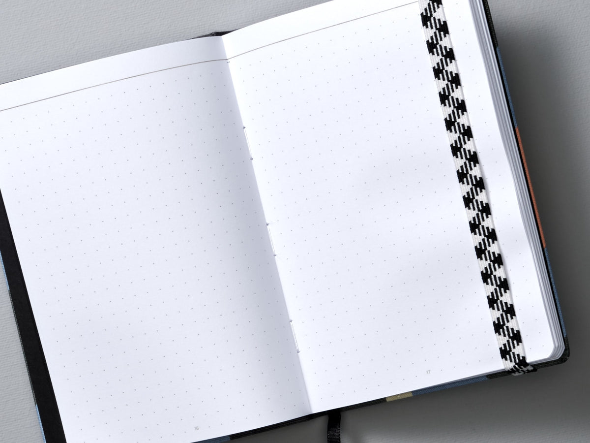 An A6 Canvas Notebook – Dot Grid from Papier Tigre with a black and white checkered pattern.