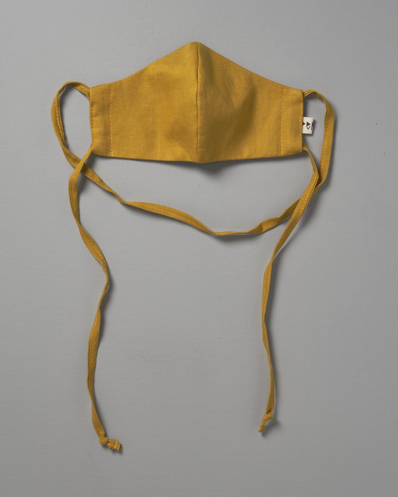 A Linen Face Mask - Citrus by Peppin hanging on a gray background.