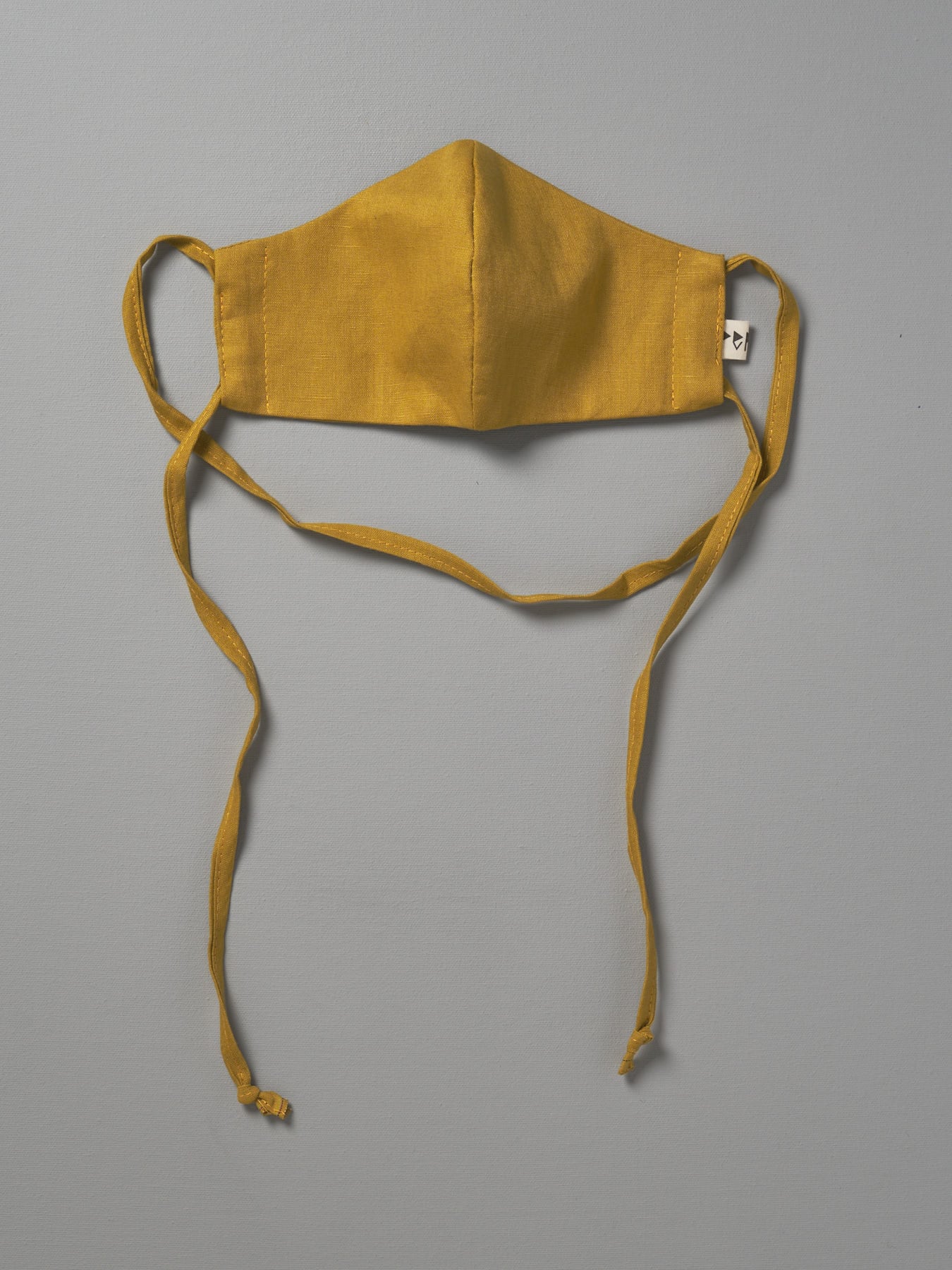 A Linen Face Mask - Citrus by Peppin hanging on a gray background.