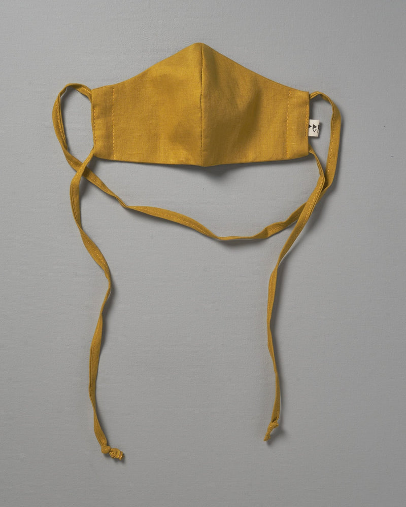 A Linen Face Mask - Citrus by Peppin hanging on a gray background.