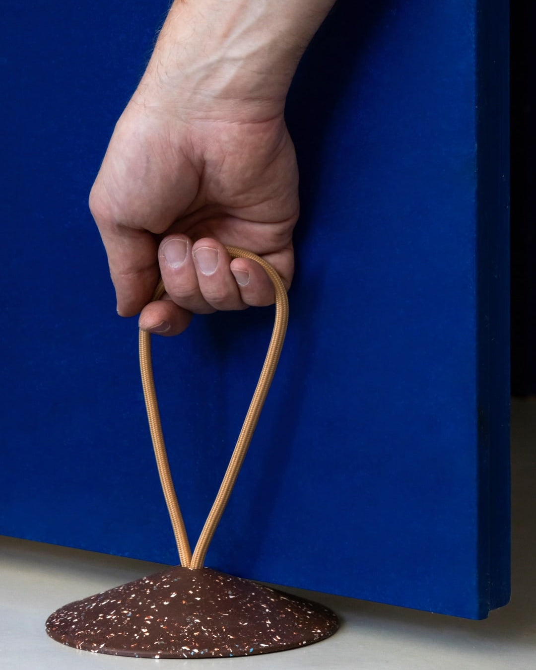 A hand is holding a STOP - Doorstop on a blue surface.