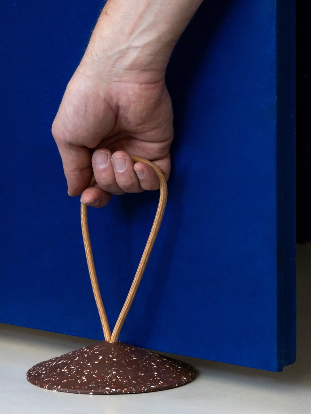 A hand is holding a STOP - Doorstop on a blue surface.