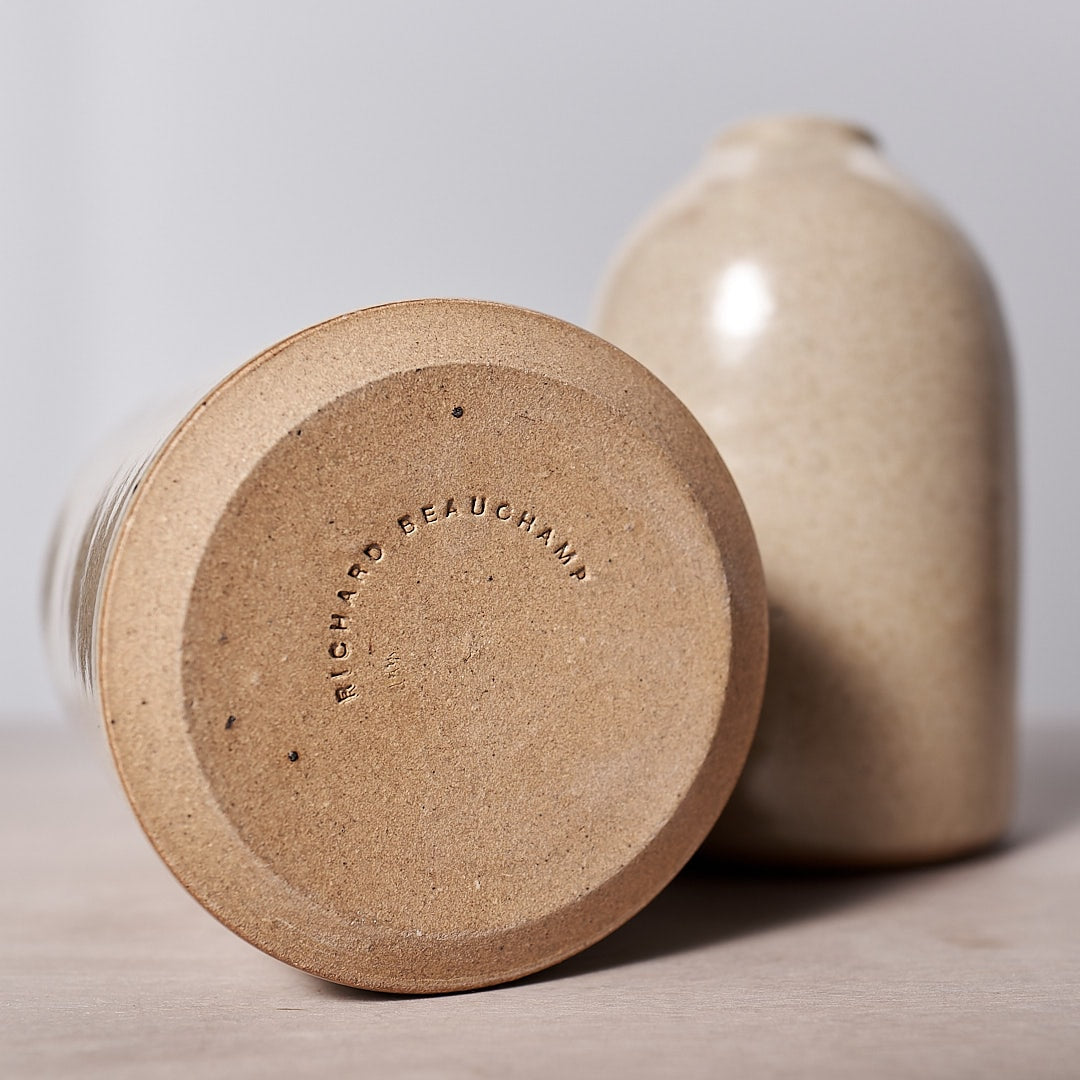 A handmade Richard Beauchamp tan jar with a lid, serving as a Small Bud Vase – Sand, sitting on a table. It is dishwasher safe.