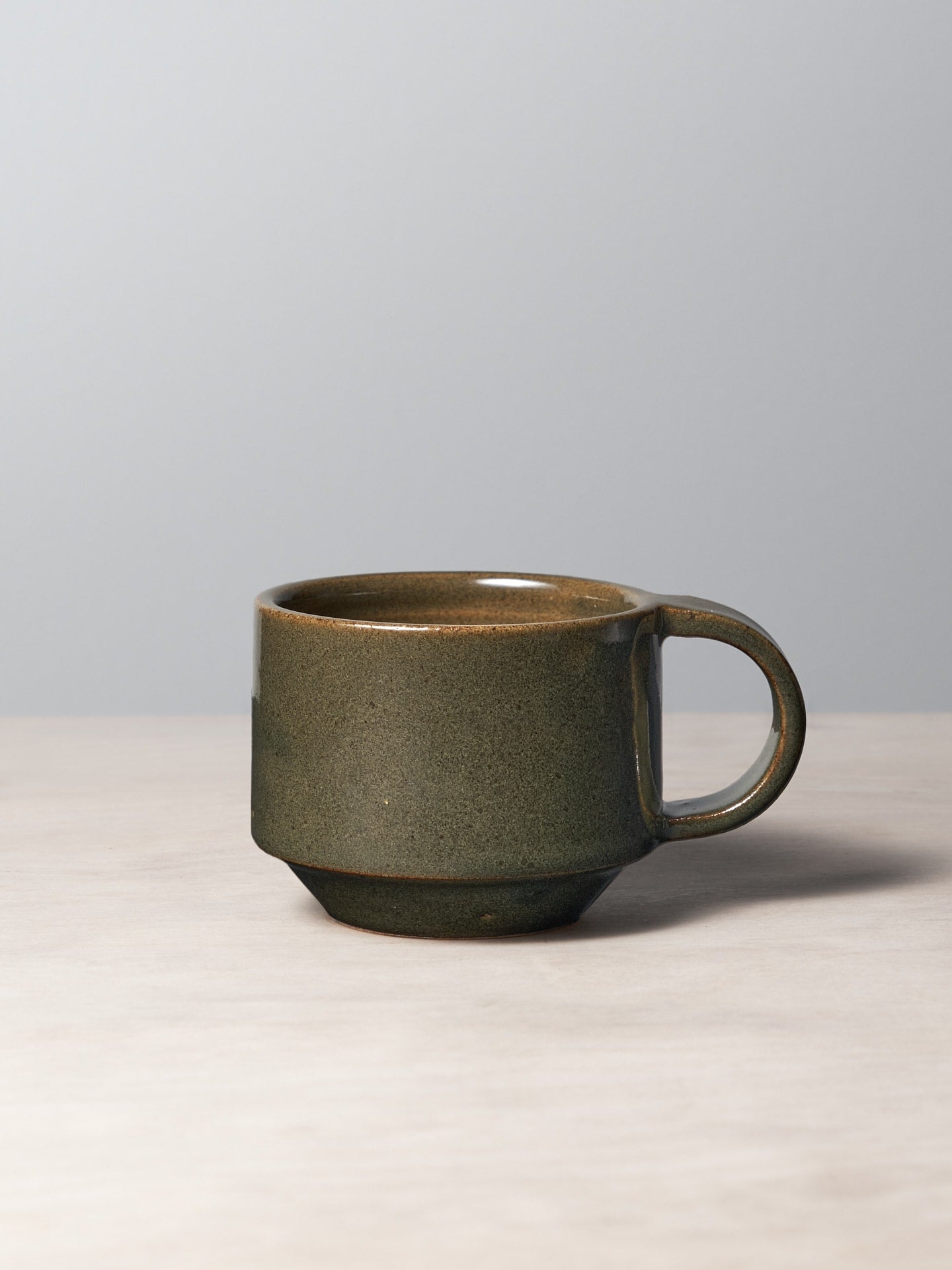 A Richard Beauchamp C-handled Stacking Mug - Green sitting on a table.
