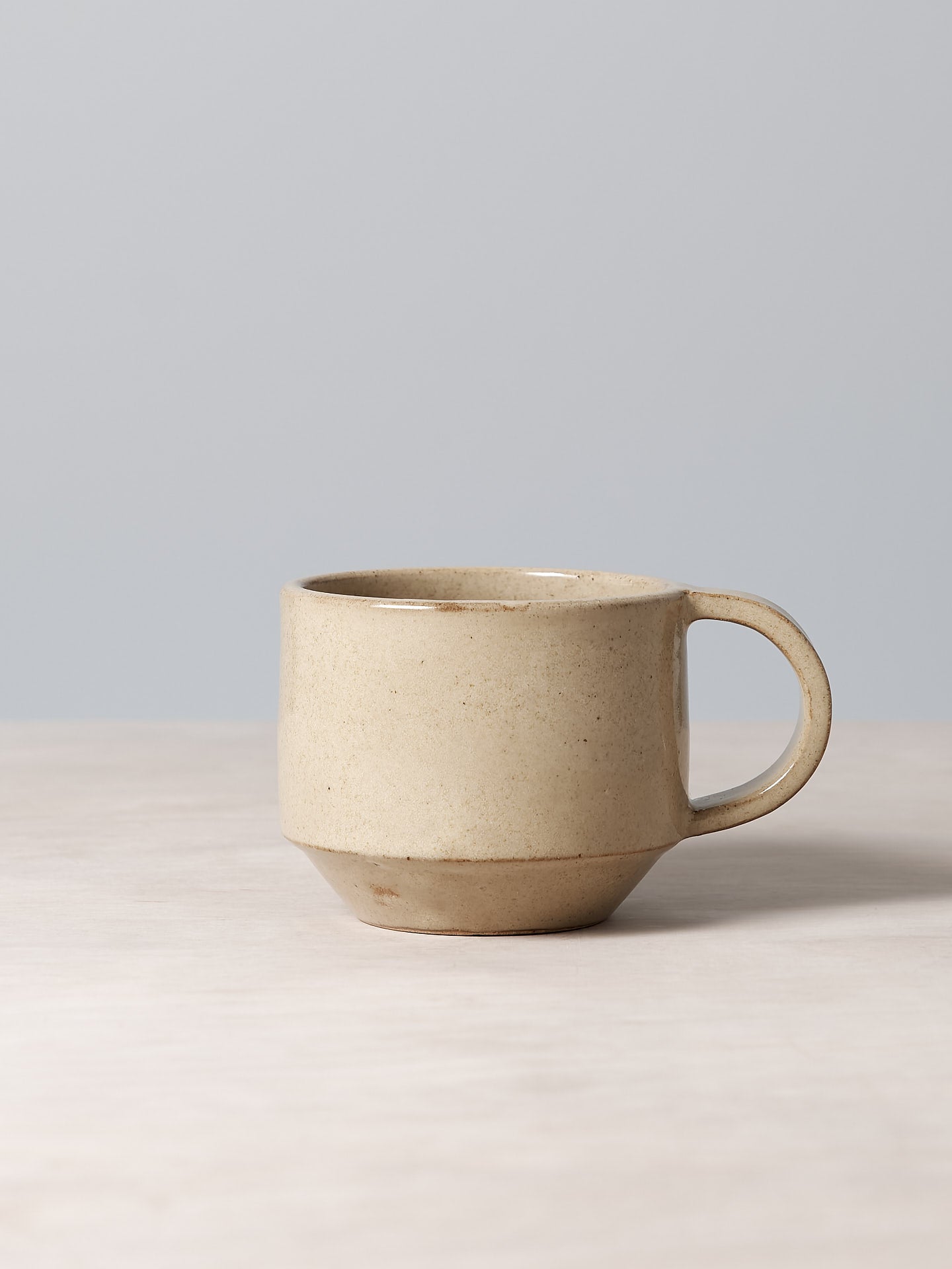 A Richard Beauchamp C-handled Stacking Mug – Sand sitting on top of a table.