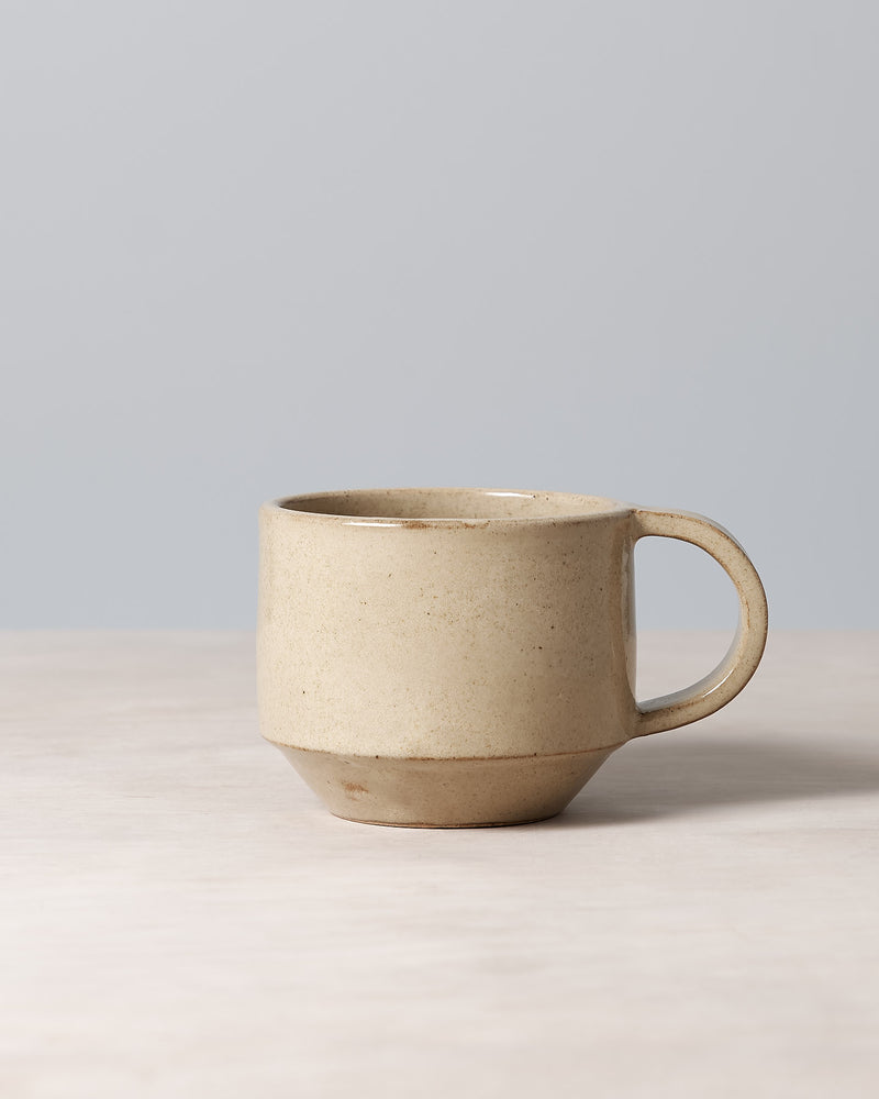 A Richard Beauchamp C-handled Stacking Mug – Sand sitting on top of a table.