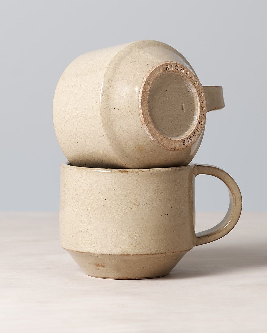 A Richard Beauchamp C-handled Stacking Mug – Sand sitting on top of a table.