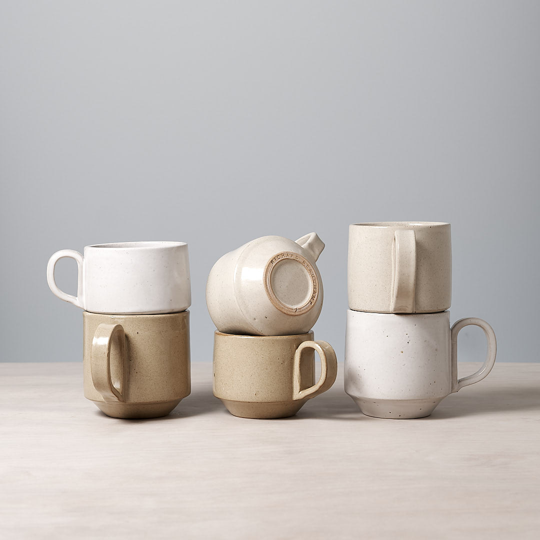 A group of Richard Beauchamp Large Stacking Mugs – Beige on a table with a gray background.