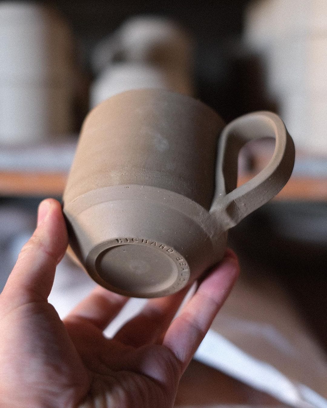A person holding up a Richard Beauchamp Large Stacking Mug - Sand with a handle.