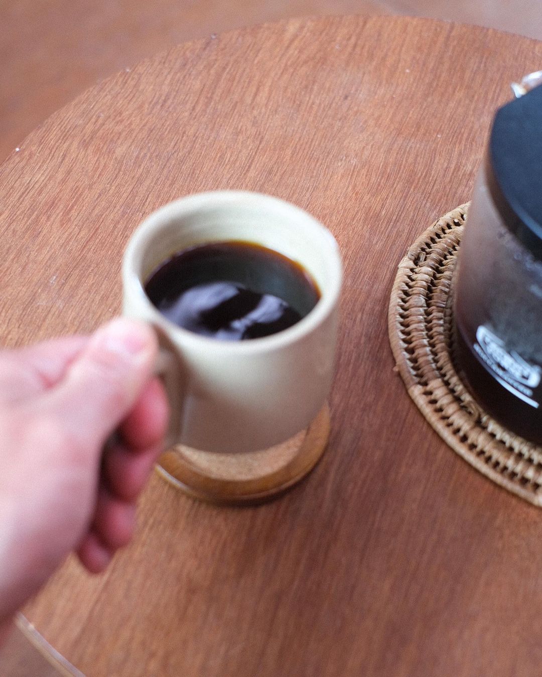 A hand holding a Richard Beauchamp Medium Stacking Mug – White next to a coffee maker.